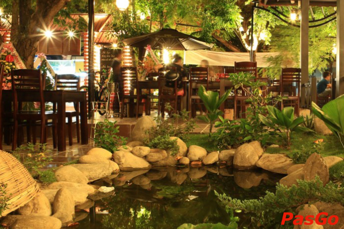 Không gian sân vườn lãng mạn về đêm với bàn ghế gỗ, đèn vàng ấm áp và tiểu cảnh hồ nước tại quán ăn ngon ở Quảng Trị.